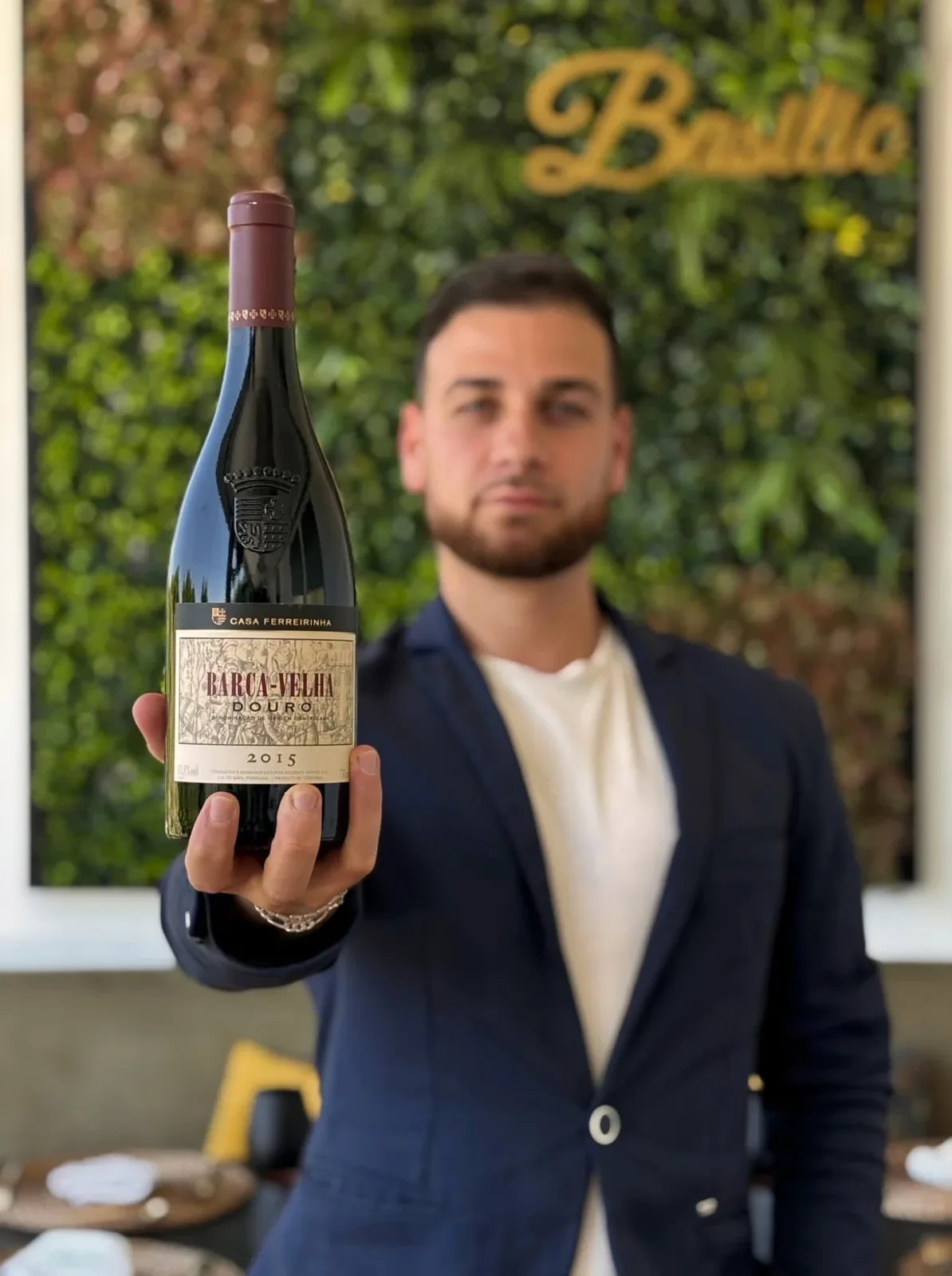 Garrafa de Barca-Velha 2015 apresentada pela equipa de sala, com a parede verde e o letreiro Basilic ao fundo