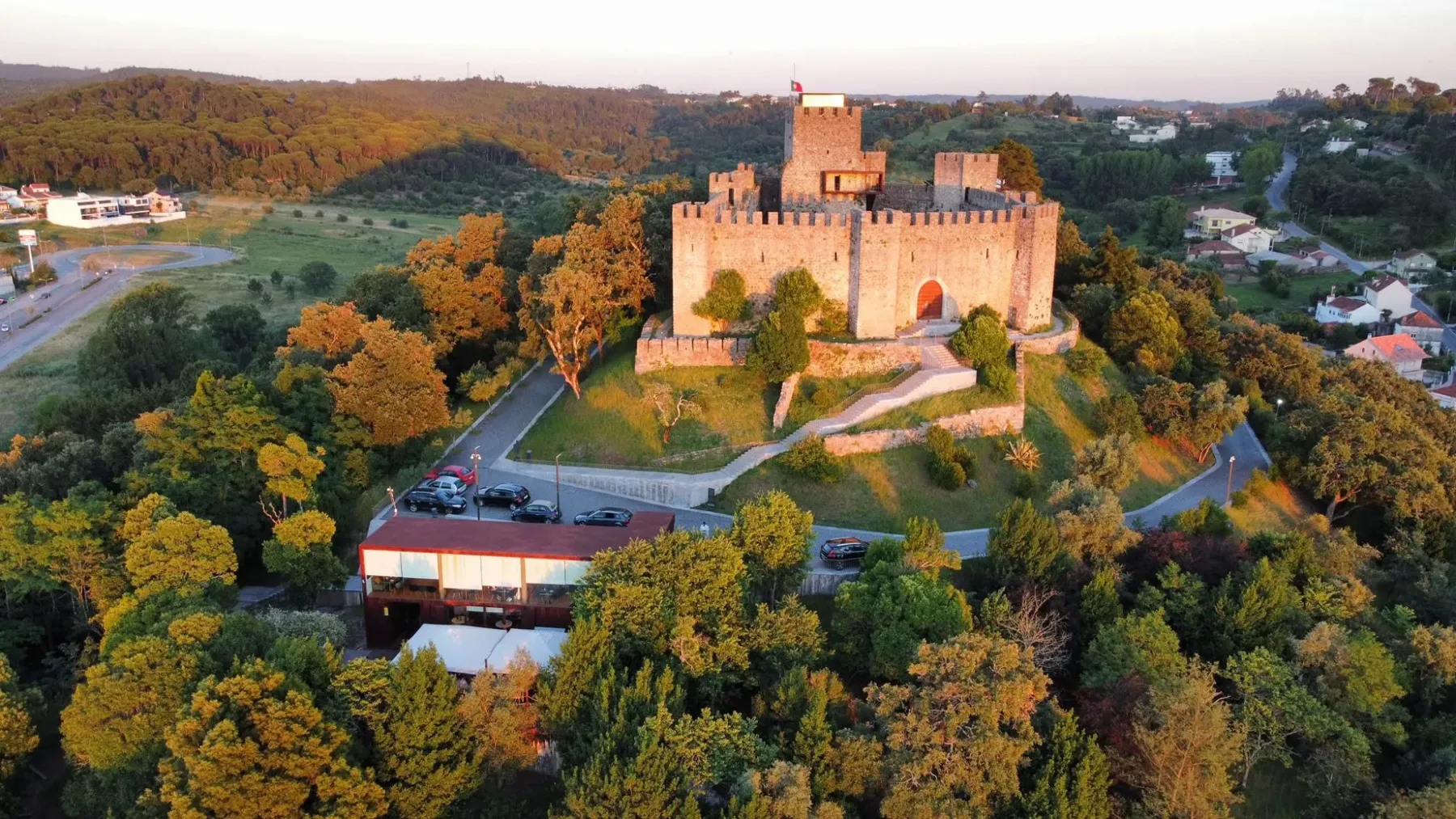 Vista aérea do Castelo de Pombal ao pôr do sol, com o edifício envidraçado do Basilic logo abaixo